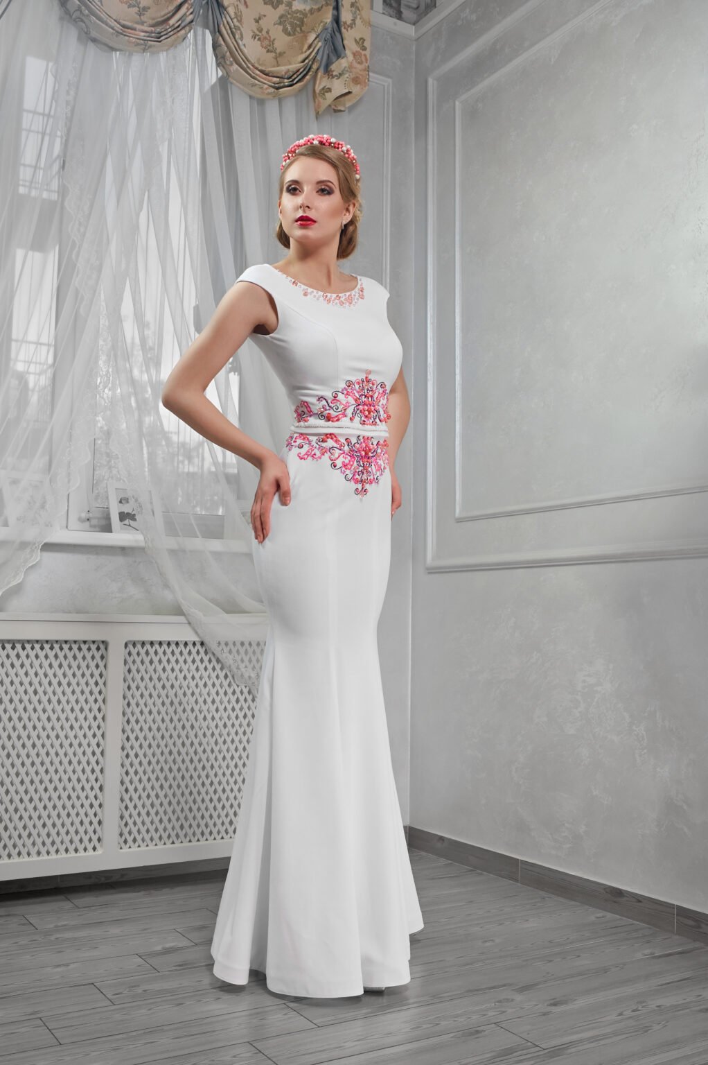 Elegant, beautiful, fashionable woman blonde in a long white dress with red embroidery, hands on hips, in room, full-length portrait, in the room, makeup.