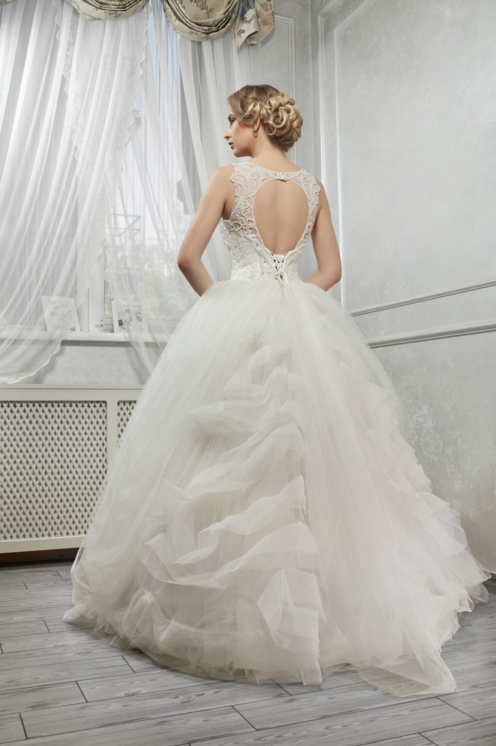 Young beautiful bride, woman in long white wedding dress on white background, hands on hips, back view.